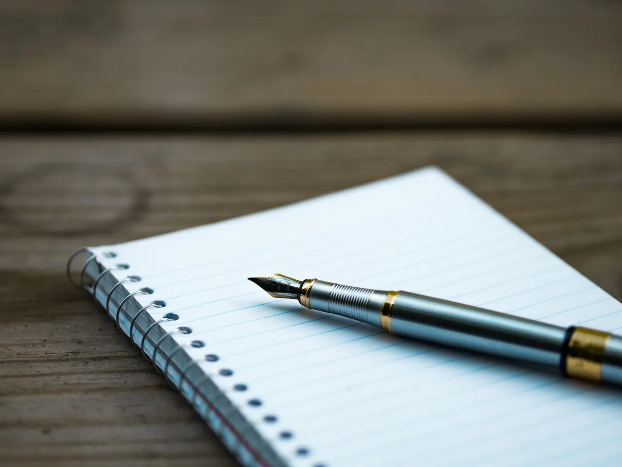 A fountain pen resting on a blank notepad on a wooden desk